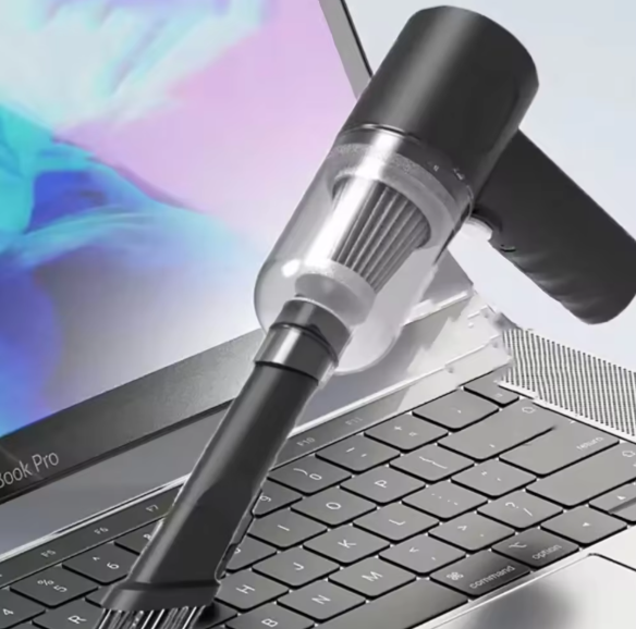 A wireless handheld vacuum cleaner being used to clean a laptop keyboard.