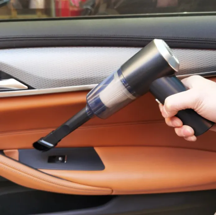 Hand using a handheld vacuum cleaner inside a car.
